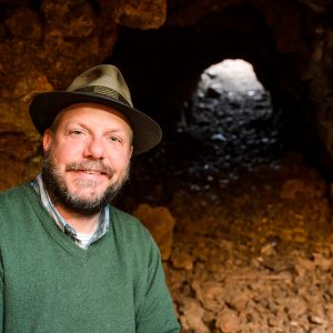 John Hawks poses in front of a cave.